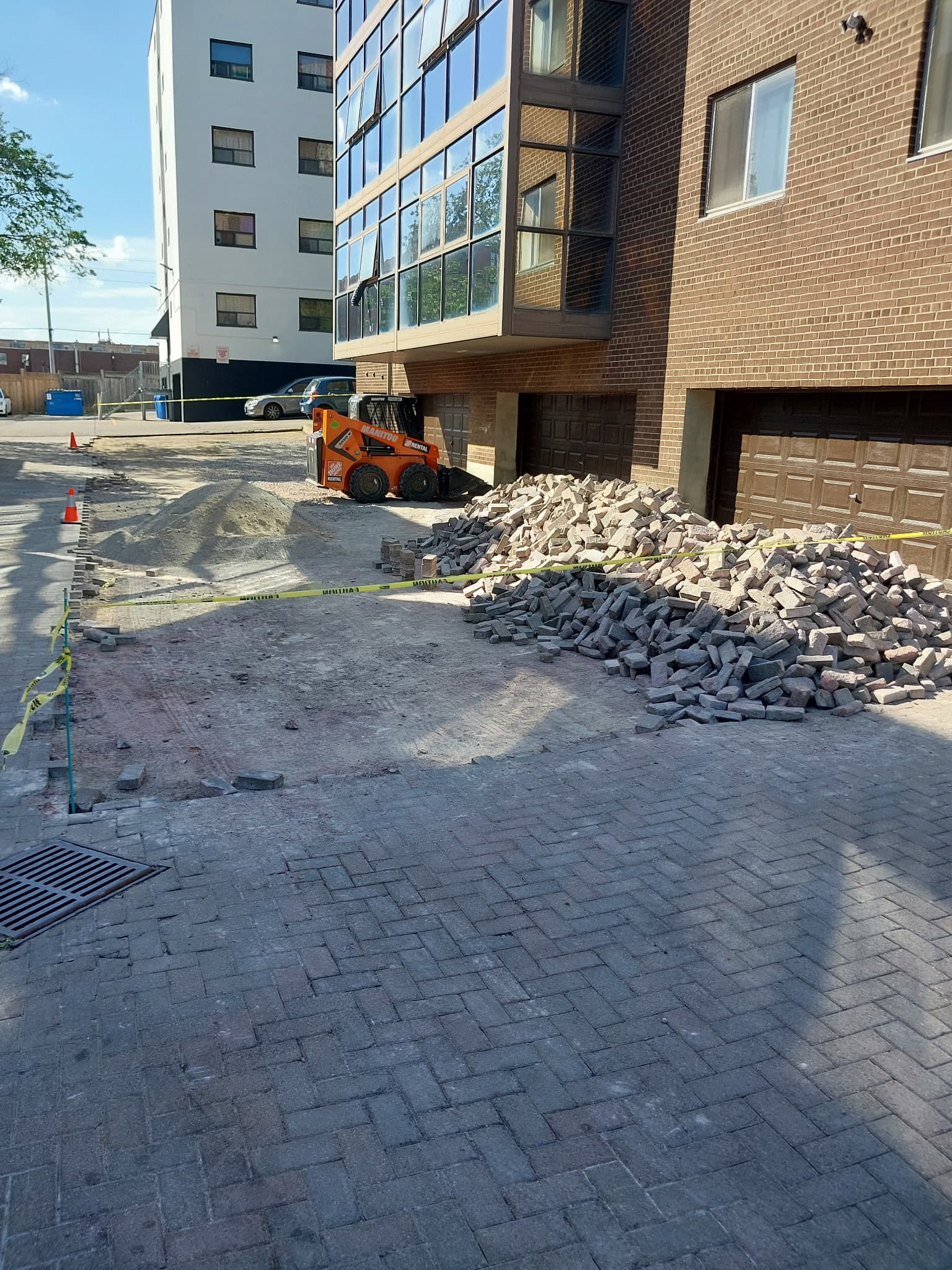 Orange skid-steer loader and a pile of grey bricks at a driveway construction site.