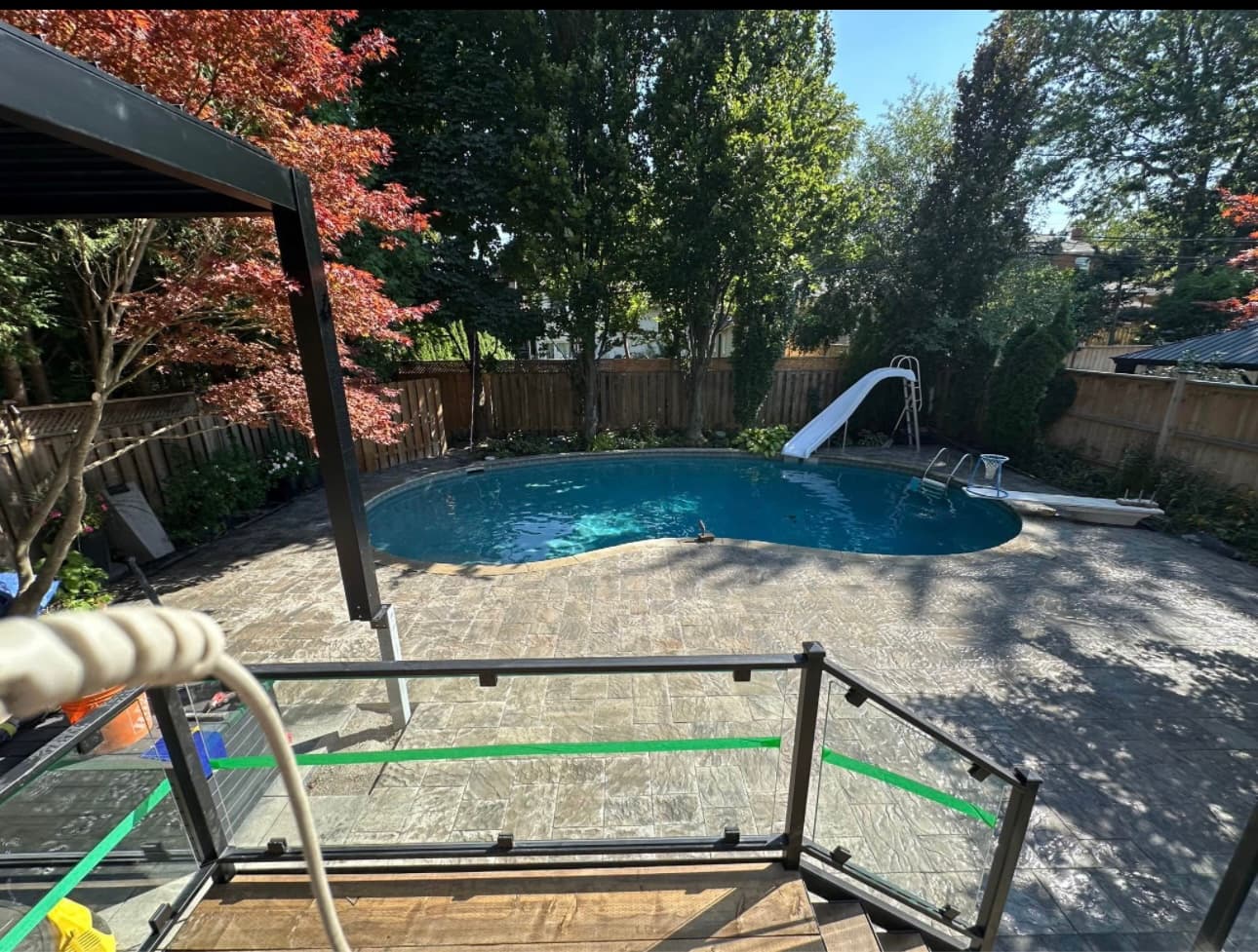 Kidney-shaped pool with slide and diving board, surrounded by stone patio and lush trees.