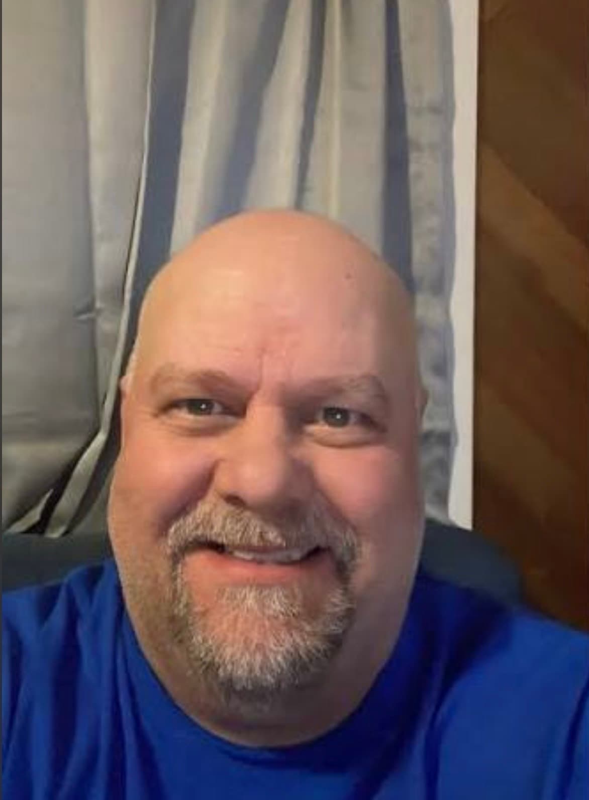 A smiling bald man with a grey goatee and mustache wearing a blue t-shirt.