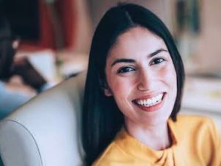 Close-up of a smiling woman with long dark hair wearing a bright yellow top.